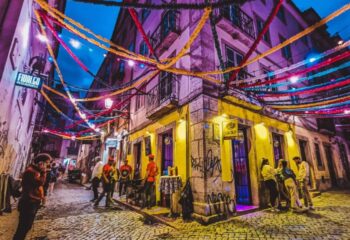 Lisbon's vibrant nightlife: A side-bar in Lisbon, Portugal, glows under colorful streamers. People gather outside, enjoying the gay travel scene.