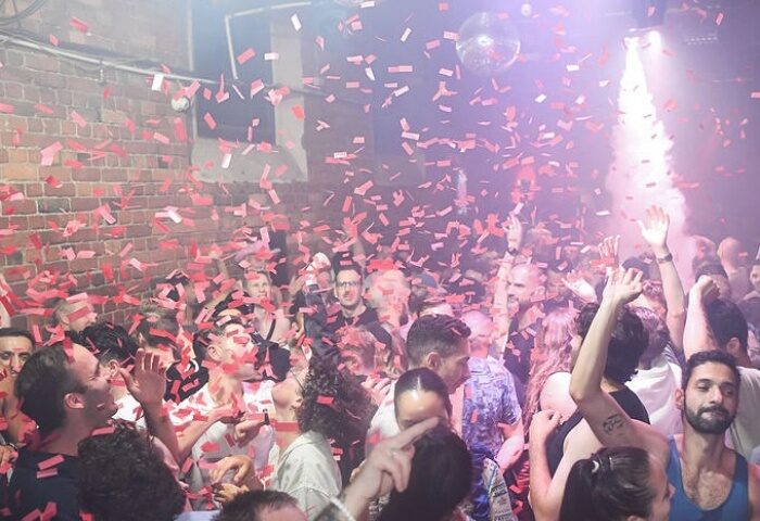 Sircuit Bar Melbourne: A lively gay bar scene with a crowd of men dancing under a disco ball and falling confetti. Nightlife and travel.