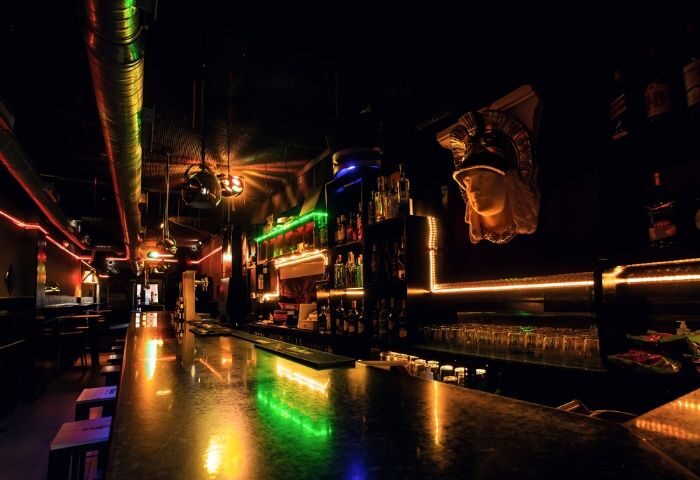 Sixta Bar, a gay bar in Madrid. Interior view of the bar with colorful lights, bottles, glasses and a Roman bust. Gay travel advice.