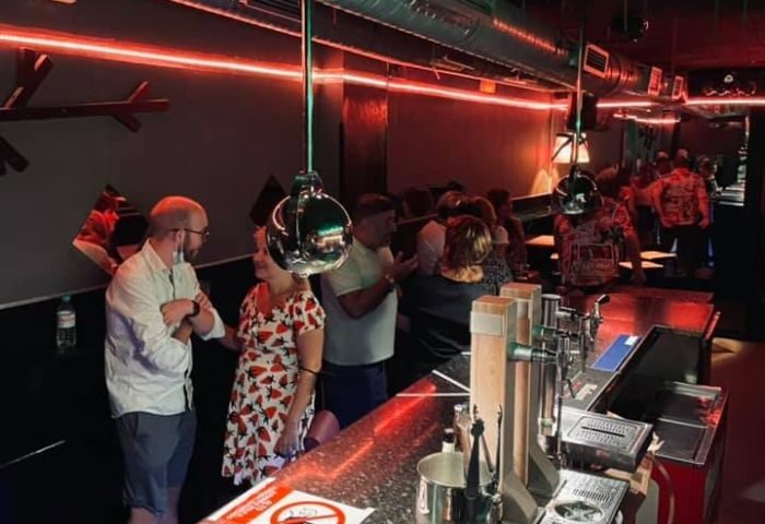Sixta Bar, a Madrid gay bar, is a popular spot for gay men. Patrons chat at the bar under red neon lights, enjoying the vibrant atmosphere.