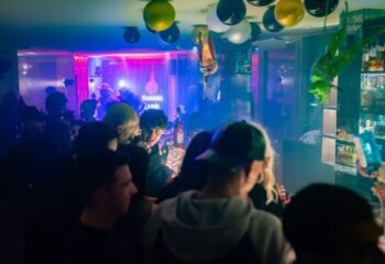 Axel Hotel Barcelona Sky Bar scene. Gay bar interior with a crowd, balloons, and bar with bottles. Nightlife at a gay-friendly hotel.