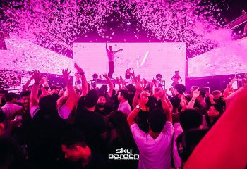 Sky Garden Bali gay dance club scene with a live DJ and music. Confetti falling, crowd cheering, and a vibrant atmosphere. Best nightlife spot.