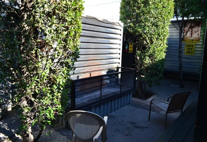 Slammer outdoor area. Grilling area with chairs, trees, and Safe Sex Only sign. Gay travel destination, providing a safe and welcoming space.
