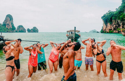 Beach Hostel slumber party. Gay-friendly hotel for solo gay travelers. Group of men drinking beer on a Thailand beach.