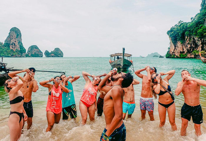 Beach Hostel slumber party. Gay-friendly hotel for solo gay travelers. Group of men drinking beer on a Thailand beach.
