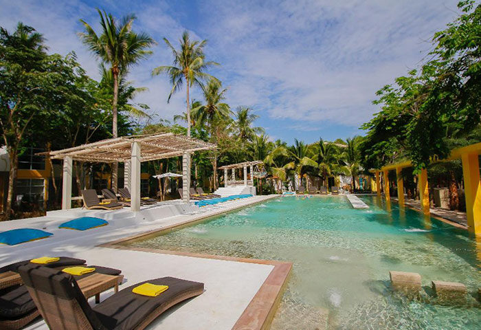 Upscale beachfront pool at gay hotel in Koh Phangan. Summer luxury resort & spa with palm trees, lounge chairs, and clear blue water.