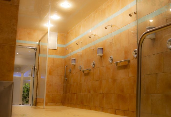 Toronto spa's shower area. Orange tiled walls with blue accents, multiple shower heads, and glass doors. Gay travel advice.