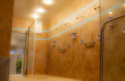 Toronto spa's shower area. Orange tiled walls with blue accents, multiple shower heads, and glass doors. Gay travel advice.