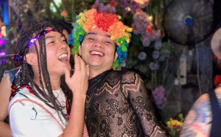 Gay travelers at Space Hair Salon & Bar, Phnom Penh. Man in rainbow wig smiles. Gay nightlife in Cambodia. LGBTQ+ travel.
