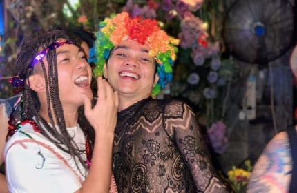 Gay travelers at Space Hair Salon & Bar, Phnom Penh. Man in rainbow wig smiles. Gay nightlife in Cambodia. LGBTQ+ travel.