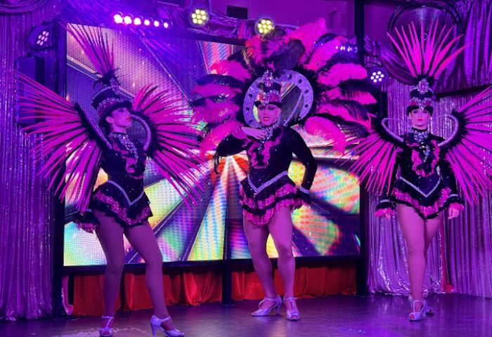 Sparkles Show Bar, a gay bar in Gran Canaria. Drag queens in pink feather costumes perform on stage under purple lights. Nightlife.