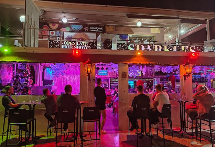 Sparkles Show Bar, a gay bar in Gran Canaria. Men sit at tables outside the bar, enjoying the open late free show, with stage lights.