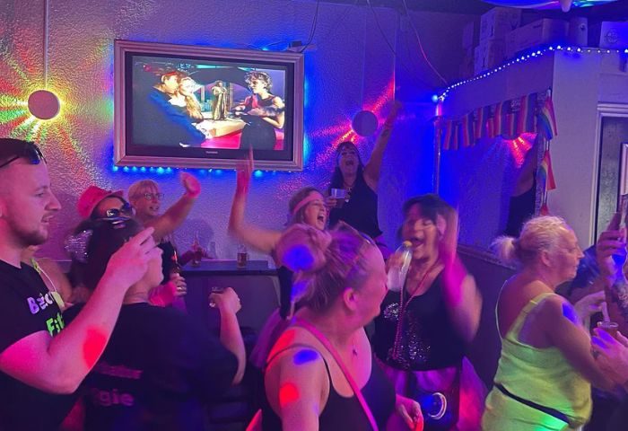 Spirit Bar Gay Bar party in Benidorm. People dancing and singing karaoke, with rainbow flags. Fun nightlife for gay men's travel.