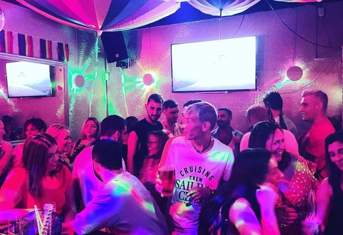 Spirit Bar gay party in Benidorm. Crowded gay bar with rainbow decorations, people drinking and socializing under colorful lights. Nightlife.
