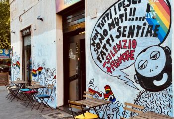 Spiritall Lounge Bar in Rome. Exterior view with tables, chairs, and a mural featuring a rainbow flag and Love is Love message. Gay travel.