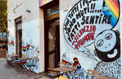 Spiritall Lounge Bar in Rome. Exterior view with tables, chairs, and a mural featuring a rainbow flag and Love is Love message. Gay travel.