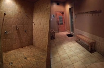 Splash Steam and Sauna gay cruising in Toronto: tiled shower area with multiple shower heads, sauna entrance, and bench in a warm-toned room.