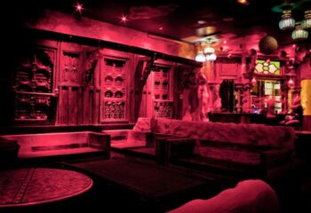 Star City, Paris: Interior view of the gay bar bathed in red light, featuring ornate wooden decor, cozy seating, and unique lighting fixtures.