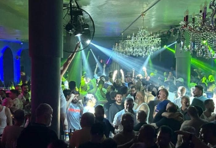 Stay Club Istanbul: A crowded gay club scene with men dancing under chandeliers and vibrant green & blue lights. Gay nightlife travel.