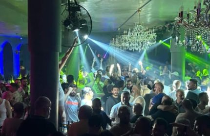 Stay Club Istanbul: A crowded gay club scene with men dancing under chandeliers and vibrant green & blue lights. Gay nightlife travel.