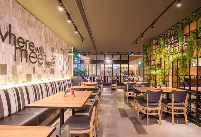 Holiday Inn Express Bangkok Sathorn's dining area. Gay-friendly hotel with modern decor, wooden tables, and lush greenery. Perfect for a smart stay.