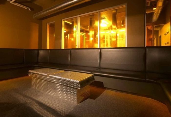 Interior of Steamworks Toronto, a gay bathhouse. Features a black leather couch and a metal coffee table.