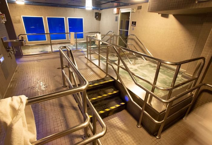 Steamworks Toronto hot tub area. Stainless steel railings lead to a bubbling hot tub. Windows with blue light filter the room. Gay sauna.