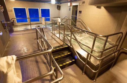 Steamworks Toronto hot tub area. Stainless steel railings lead to a bubbling hot tub. Windows with blue light filter the room. Gay sauna.
