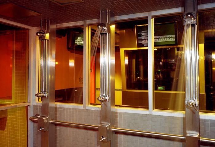 Showers at Steamworks Toronto, a popular gay sauna. Stainless steel fixtures, tiled walls, and glass partitions create a sleek, modern spa.