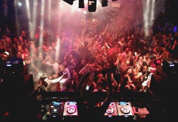 Montreal gay party at Stereo Bar. DJ playing music to a crowd of people dancing with hands in the air, enjoying the nightlife.
