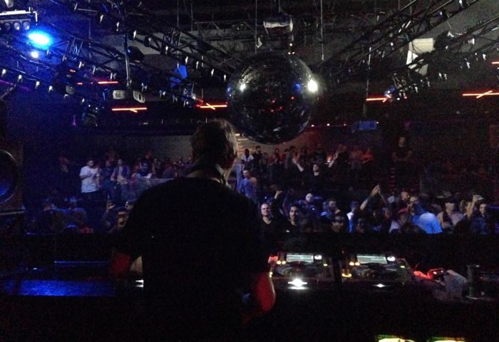Montreal gay party at Stereo Bar. DJ faces the crowd under a disco ball. Nightlife scene for gay men's travel advice.