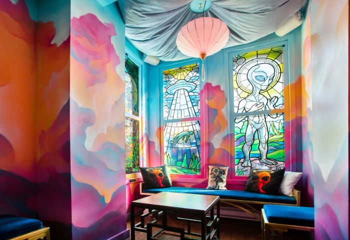 Storm Crow Manor in Toronto: Quirky room with colorful murals, stained glass windows featuring aliens, and cozy seating. Gay travel spot.