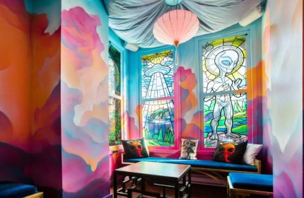 Storm Crow Manor in Toronto: Quirky room with colorful murals, stained glass windows featuring aliens, and cozy seating. Gay travel spot.