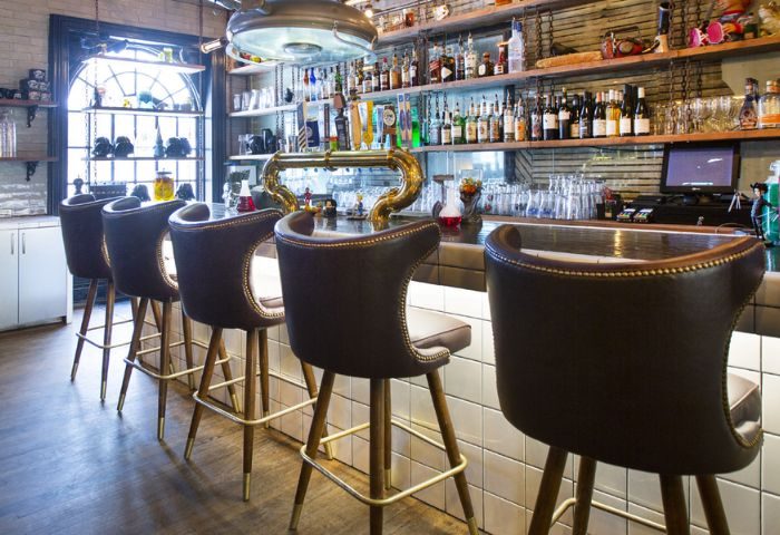 Storm Crow Manor bar in Toronto. Leather bar stools line the counter. Shelves are stocked with liquor bottles. Gay travel advice.