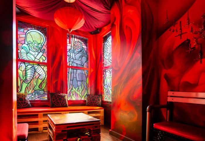Storm Crow Manor in Toronto, Canada. Red themed room with stained glass windows, pentagram pillows, and a wooden pallet table.