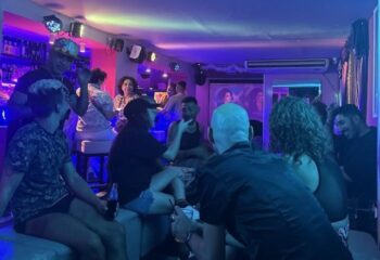 Inside Strass Barcelona Gay Bar: A vibrant scene with men socializing under neon lights. A popular spot for gay men's travel in Barcelona.