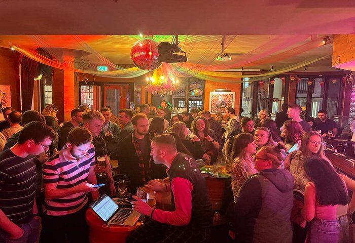 Street 66 Gay Bar in Dublin 2. A lively, crowded gay bar scene with a disco ball, colorful lighting, and people socializing. Dublin gay nightlife.