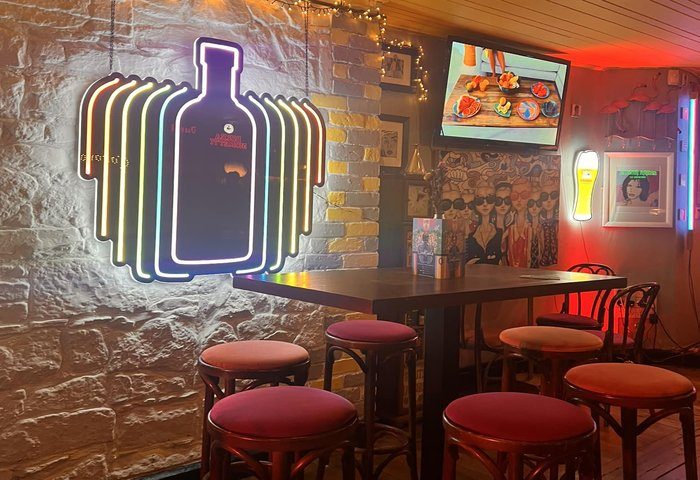 Interior of Street 66 Gay Bar in Dublin, Ireland. Neon bottle sign, high table with stools, and TV screen. Gay travel destination.