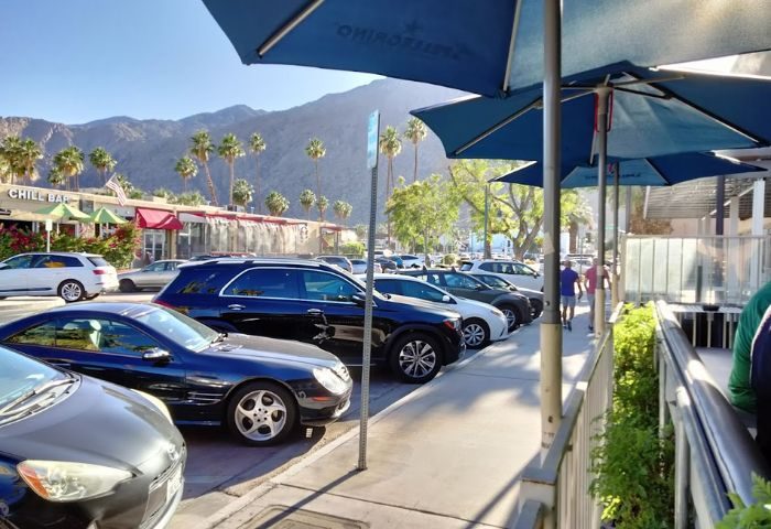 Streetbar parking. Cars parked near a gay-friendly bar with mountains and palm trees in the background. Outdoor seating with umbrellas.