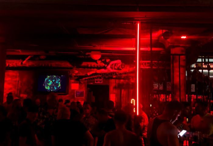 Inside Strong Construction gay cruise club in Gran Canaria. Red lighting, crowd of men, screen, bar. Gay nightlife travel.