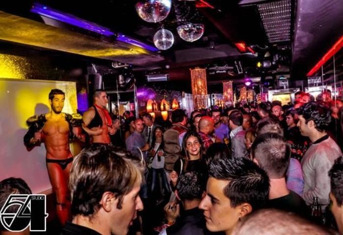 Studio 54 Madrid gay bar scene. Crowd of people, disco balls, and two shirtless men in underwear on a stage. Gay travel advice.