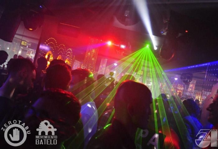 Studio 54 Madrid gay bar scene. Crowd of men under green and red lights. Nightlife in Madrid for gay travelers.