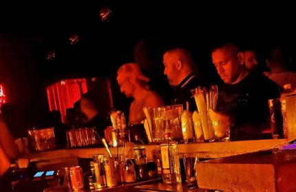 Studs Bear Bar, a gay place in Puerto Vallarta. Men at the bar in a dimly lit, red-toned gay bar. Nightlife scene.