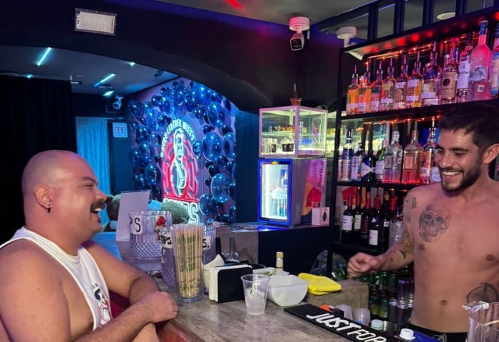 Studs Bear Bar: A gay bear enjoys a drink at the bar with a smiling bartender in Puerto Vallarta. Nightlife for gay men.