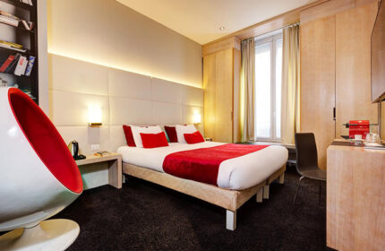 Hotel Elixir, a stylish gay honeymoon hotel in Paris' Marais gayborhood. Modern room with red accents, comfy bed, and unique chair.
