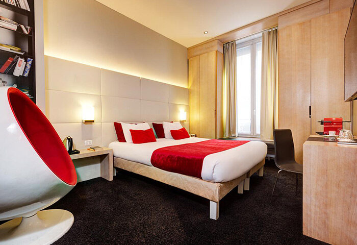 Hotel Elixir, a stylish gay honeymoon hotel in Paris' Marais gayborhood. Modern room with red accents, comfy bed, and unique chair.