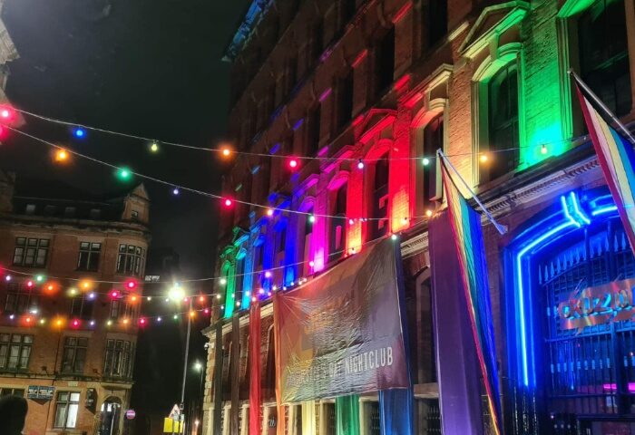 Manchester's Sub 101 nightclub, a gay travel destination, is lit with rainbow colors. Pride flags and string lights adorn the building's exterior.