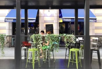 Sui Generis bar in Milan, Italy. Outdoor seating area, a popular gay-friendly spot. Blue awnings & lush greenery. Gay travel advice.