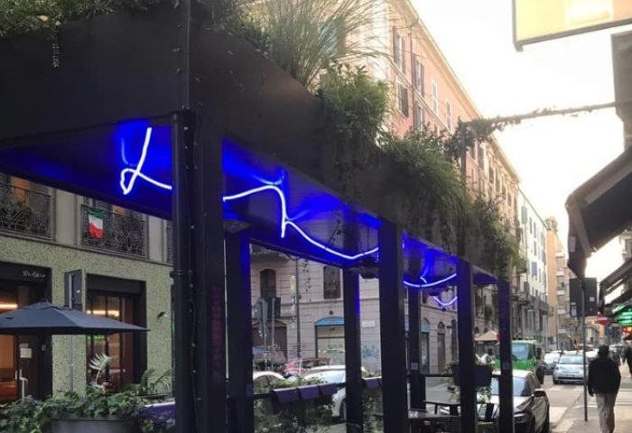 Sui Generis Milan: Outdoor seating area with blue neon lighting. Milan's street view. Gay travel advice, stylish Italian cafe.