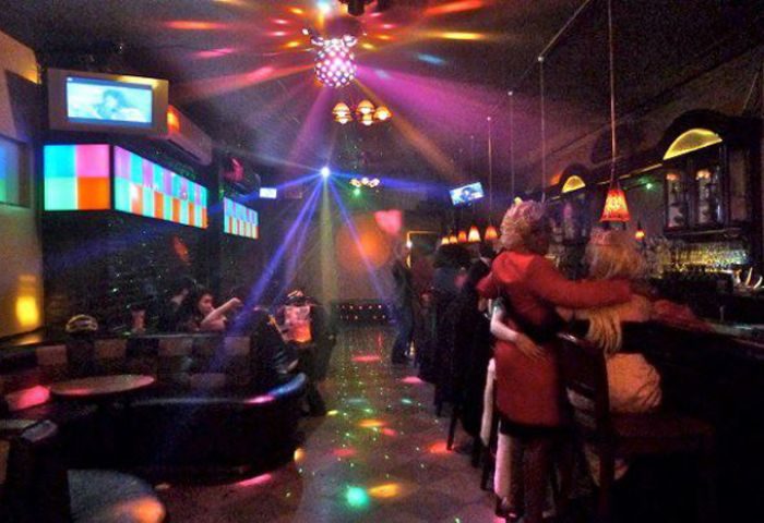 Inside Suite, a gay bar/pub in NYC. Couples dance under disco lights. TVs & colorful panels adorn the walls. A vibrant nightlife scene.